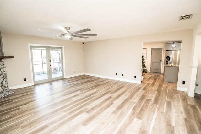 unfurnished living room featuring ceiling fan, light hardwood / wood-style flooring, a stone fireplace, and french doors