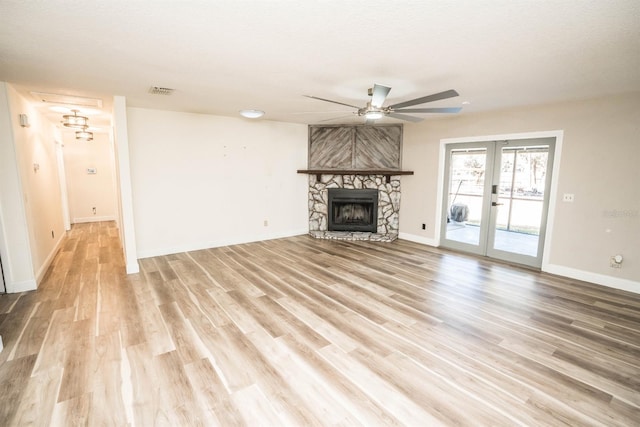 unfurnished living room with a fireplace, light wood-type flooring, ceiling fan, and french doors