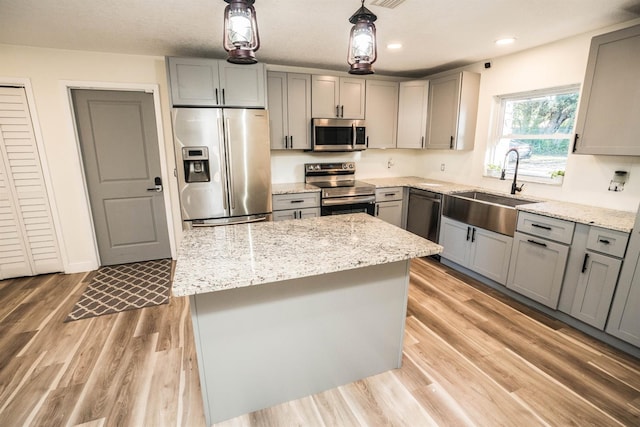 kitchen with a center island, stainless steel appliances, sink, hanging light fixtures, and gray cabinets