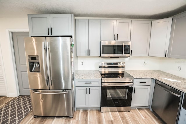 kitchen featuring appliances with stainless steel finishes, light stone countertops, gray cabinets, a textured ceiling, and light hardwood / wood-style floors