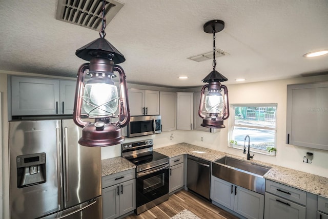 kitchen with light stone countertops, appliances with stainless steel finishes, decorative light fixtures, light hardwood / wood-style floors, and gray cabinets