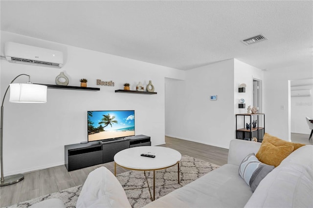 living room featuring hardwood / wood-style flooring, a wall mounted AC, and a textured ceiling