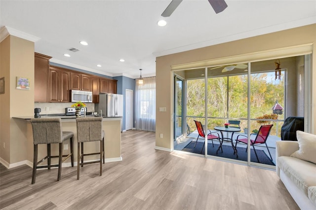 kitchen with a kitchen bar, appliances with stainless steel finishes, decorative light fixtures, ornamental molding, and kitchen peninsula