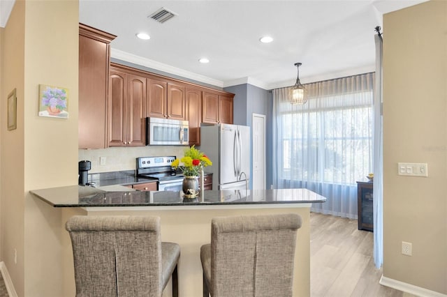 kitchen featuring kitchen peninsula, dark stone counters, hanging light fixtures, and appliances with stainless steel finishes