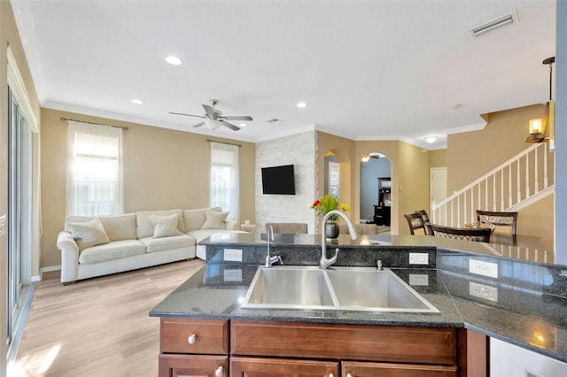 kitchen featuring dark stone countertops, sink, light wood-type flooring, ceiling fan, and crown molding