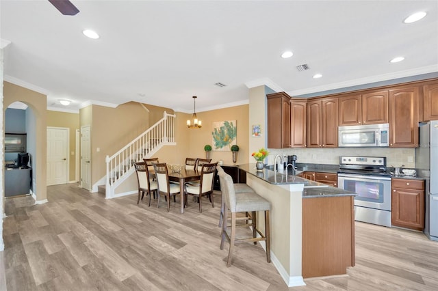 kitchen featuring decorative light fixtures, kitchen peninsula, light hardwood / wood-style flooring, and stainless steel appliances