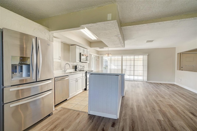 kitchen with light hardwood / wood-style floors, appliances with stainless steel finishes, a chandelier, white cabinets, and sink