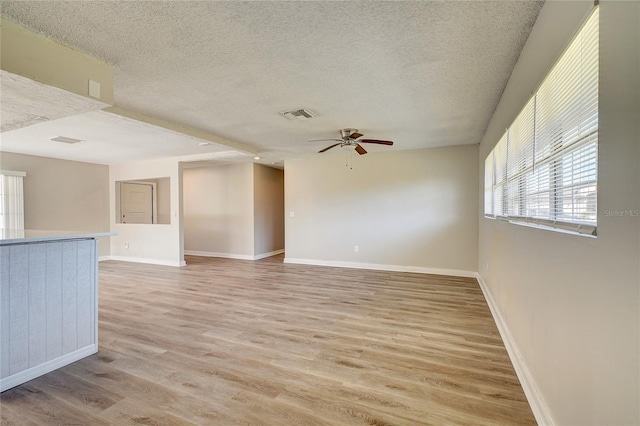 spare room with light wood-type flooring, ceiling fan, and a textured ceiling