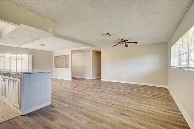 unfurnished living room featuring light wood-type flooring, ceiling fan, and a textured ceiling