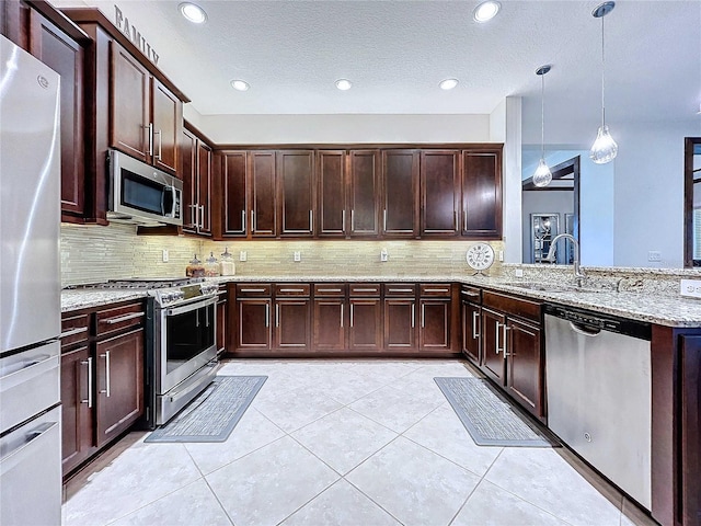 kitchen featuring pendant lighting, sink, light stone counters, kitchen peninsula, and stainless steel appliances