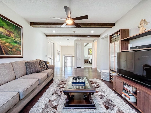 living room with dark hardwood / wood-style flooring, ceiling fan, beam ceiling, and a textured ceiling