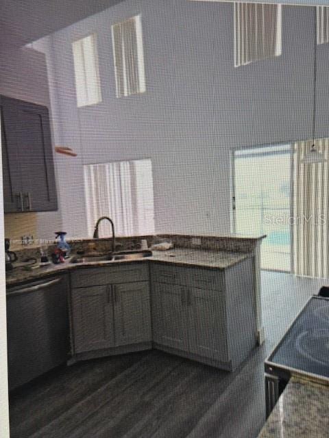 kitchen featuring dark wood-type flooring, backsplash, stainless steel dishwasher, and sink