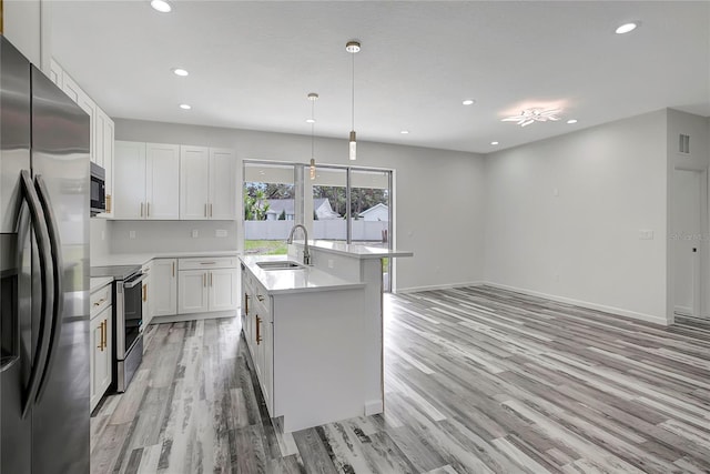 kitchen with pendant lighting, sink, appliances with stainless steel finishes, white cabinets, and a center island with sink