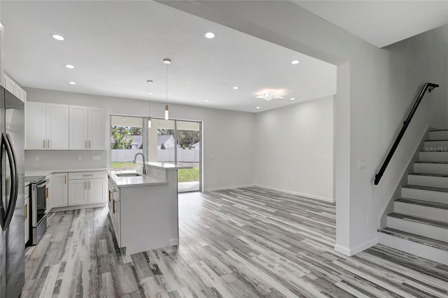 kitchen featuring electric stove, sink, hanging light fixtures, white cabinets, and a center island with sink