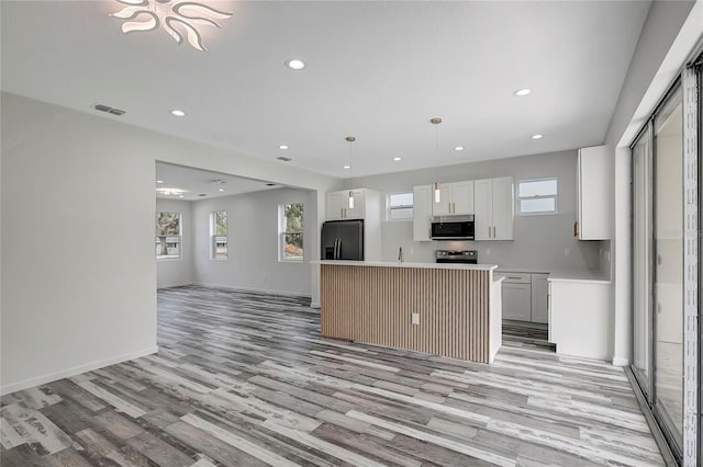 kitchen with stainless steel refrigerator with ice dispenser, white cabinetry, hanging light fixtures, a kitchen island, and light hardwood / wood-style floors