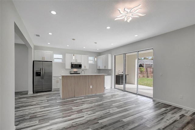 kitchen featuring white cabinetry, appliances with stainless steel finishes, a kitchen island with sink, and hanging light fixtures