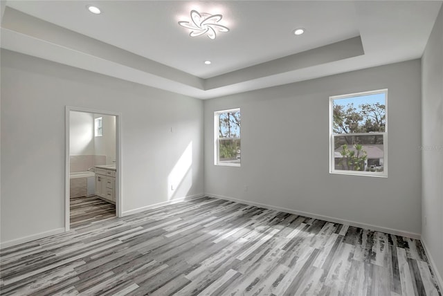 unfurnished bedroom featuring multiple windows, connected bathroom, and a raised ceiling