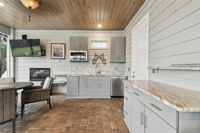 kitchen with dishwasher, sink, light stone countertops, wood ceiling, and wooden walls