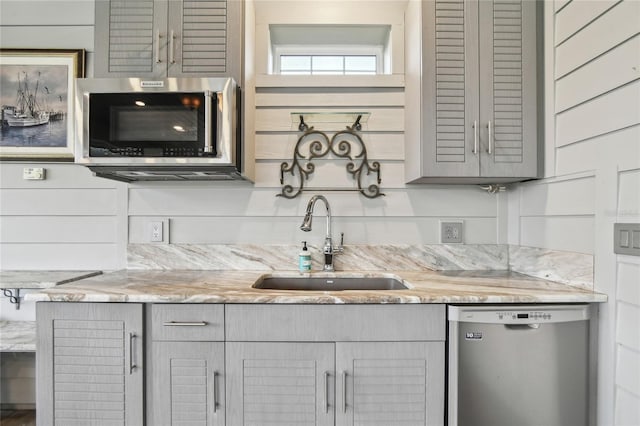 kitchen with sink, gray cabinets, wooden walls, and appliances with stainless steel finishes