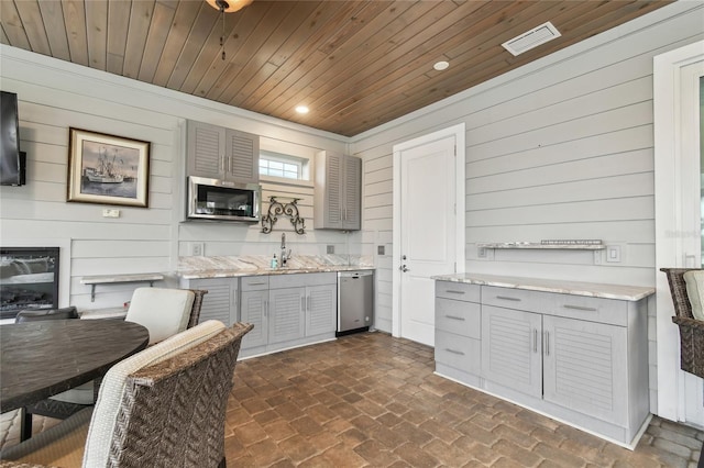 kitchen with wooden ceiling, gray cabinets, wood walls, and stainless steel appliances