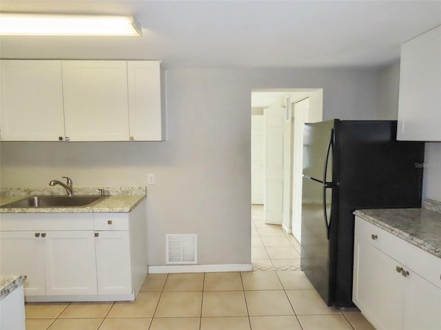 kitchen featuring white cabinetry, black fridge, sink, and light tile patterned floors