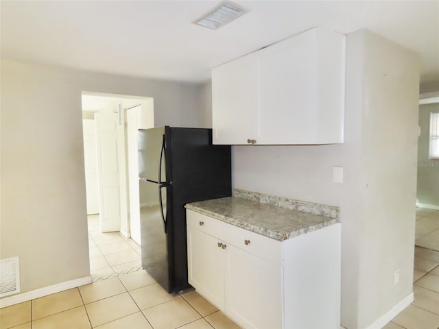 kitchen with white cabinetry, light tile patterned floors, and black fridge