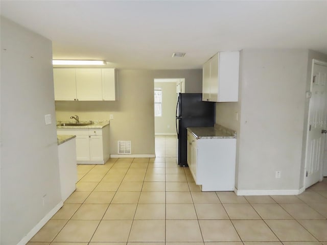 kitchen featuring black refrigerator, light tile patterned floors, sink, and white cabinets