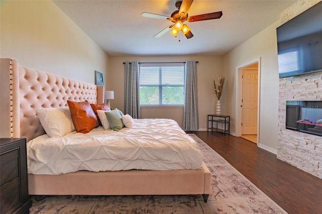 bedroom with ceiling fan, dark hardwood / wood-style flooring, and a stone fireplace