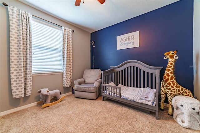 carpeted bedroom featuring multiple windows, ceiling fan, and a nursery area