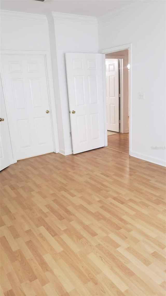 unfurnished bedroom with a closet, crown molding, and light wood-type flooring