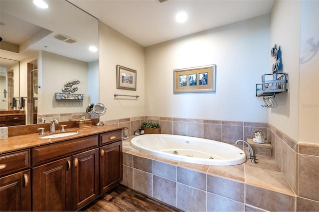 bathroom featuring hardwood / wood-style flooring, vanity, and tiled bath