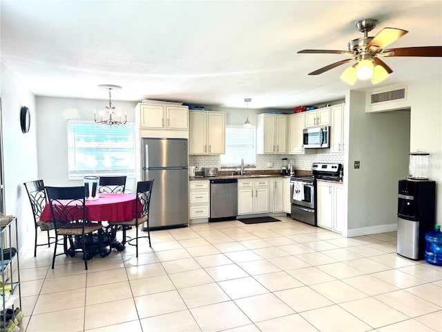 kitchen featuring light tile patterned flooring, appliances with stainless steel finishes, pendant lighting, ceiling fan with notable chandelier, and tasteful backsplash