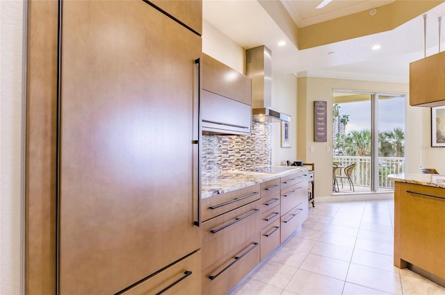 kitchen with wall chimney range hood, ornamental molding, light stone countertops, and decorative backsplash