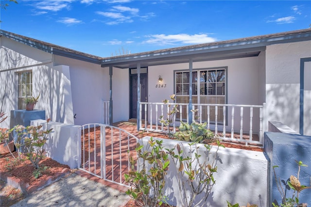 doorway to property featuring a porch, a gate, and stucco siding