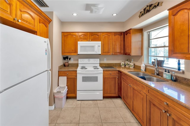 kitchen featuring white appliances, light tile patterned floors, brown cabinetry, and a sink