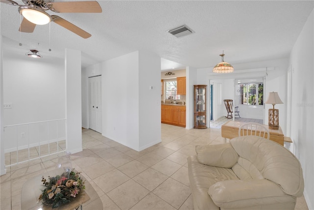 living room featuring a textured ceiling, light tile patterned floors, visible vents, and baseboards