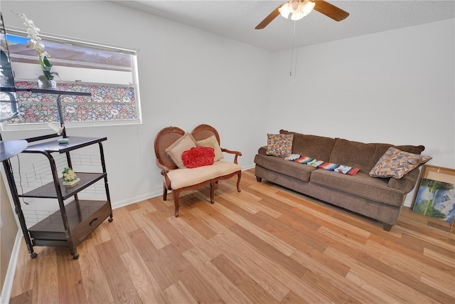 living area with light wood-type flooring, a textured ceiling, baseboards, and a ceiling fan