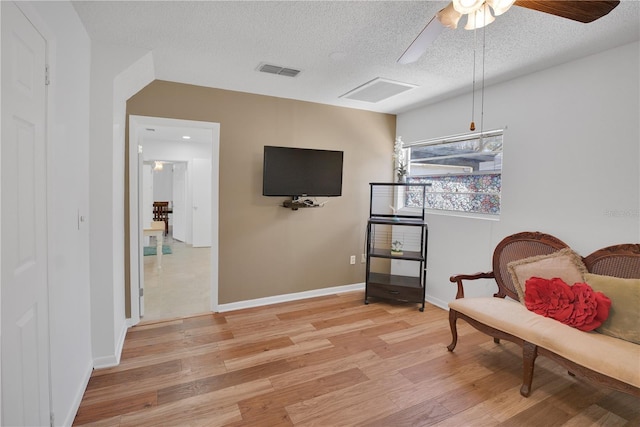 sitting room featuring a textured ceiling, baseboards, visible vents, and light wood-style floors