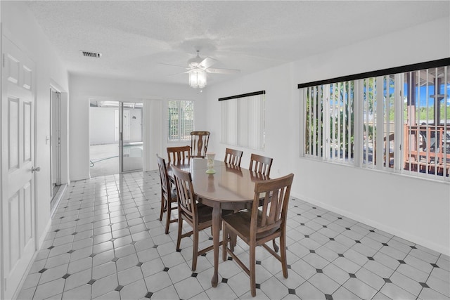 dining room featuring baseboards, ceiling fan, visible vents, and a textured ceiling