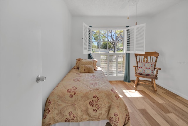 bedroom with light wood-style floors, a textured ceiling, and baseboards