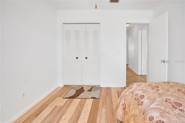 bedroom with baseboards, a closet, visible vents, and wood finished floors