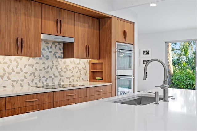 kitchen featuring black electric cooktop, stainless steel double oven, sink, and decorative backsplash