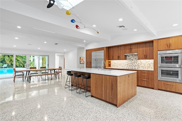 kitchen with sink, a breakfast bar area, a large island with sink, appliances with stainless steel finishes, and decorative backsplash