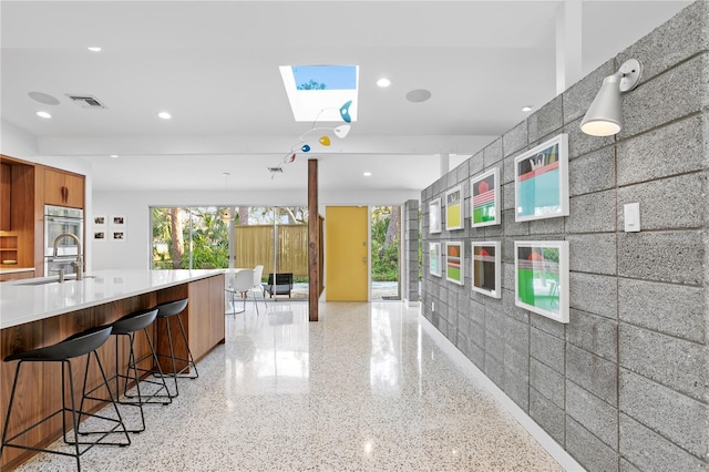 kitchen with sink, double oven, a kitchen bar, and a skylight