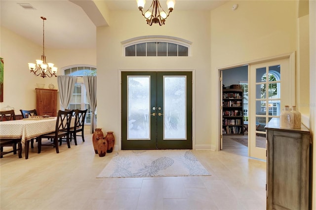 entryway featuring a towering ceiling, light tile patterned floors, a notable chandelier, and french doors