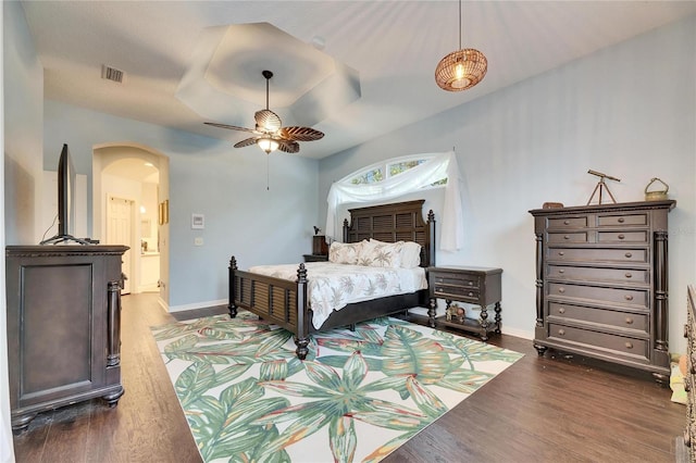 bedroom with ceiling fan, ensuite bath, dark wood-type flooring, and a tray ceiling