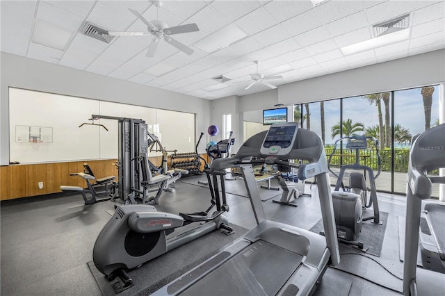 workout area featuring ceiling fan, a paneled ceiling, and wooden walls