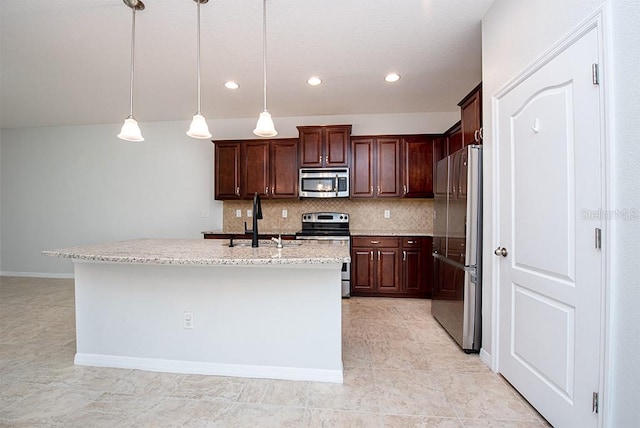 kitchen with appliances with stainless steel finishes, backsplash, hanging light fixtures, a kitchen island with sink, and light stone counters