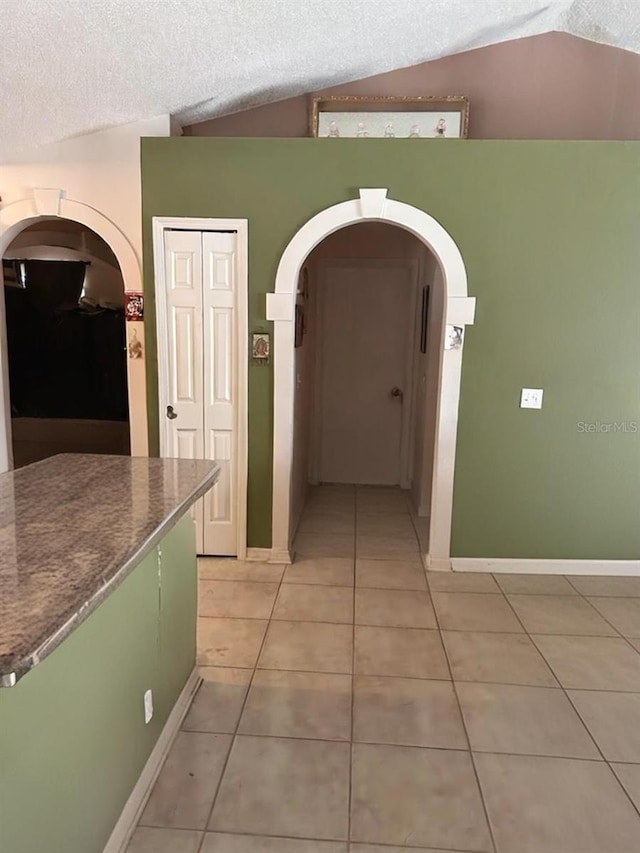 hallway featuring lofted ceiling, a textured ceiling, and light tile patterned floors