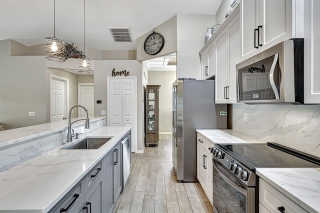 kitchen with pendant lighting, sink, white cabinetry, light stone counters, and stainless steel appliances